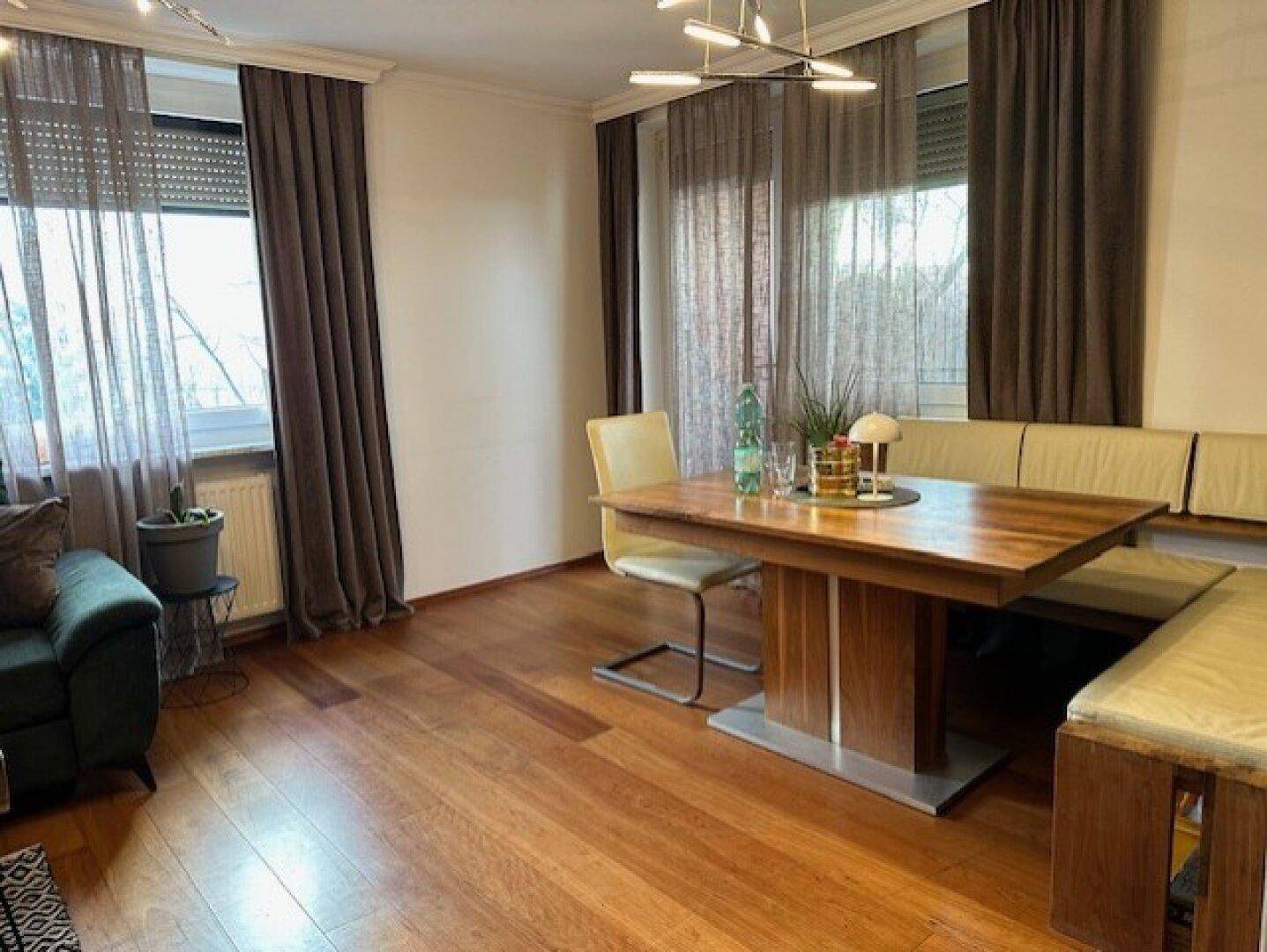 Heller Essbereich mit großem Holztisch, Sitzbank und Parkettboden.