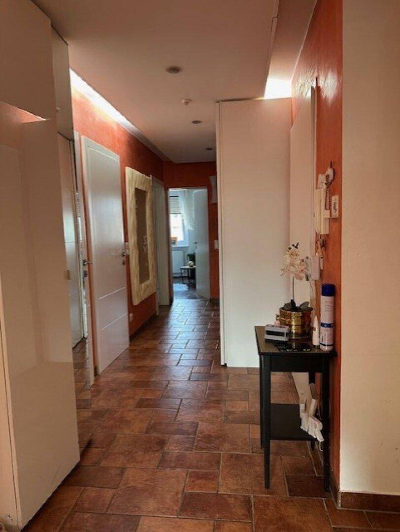 Langer Flur mit Terrakotta-Fliesenboden, orangefarbenen Wänden und Einbauschränken.