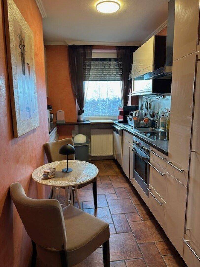 Schmale Küche mit hellen Schränken, Essbereich und Terrakotta-Fliesenboden.