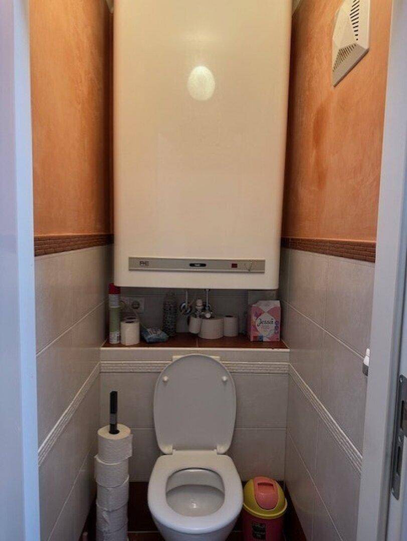 Kleines Gäste-WC mit Wand-WC, Boiler und Fliesen an Wänden und Boden.