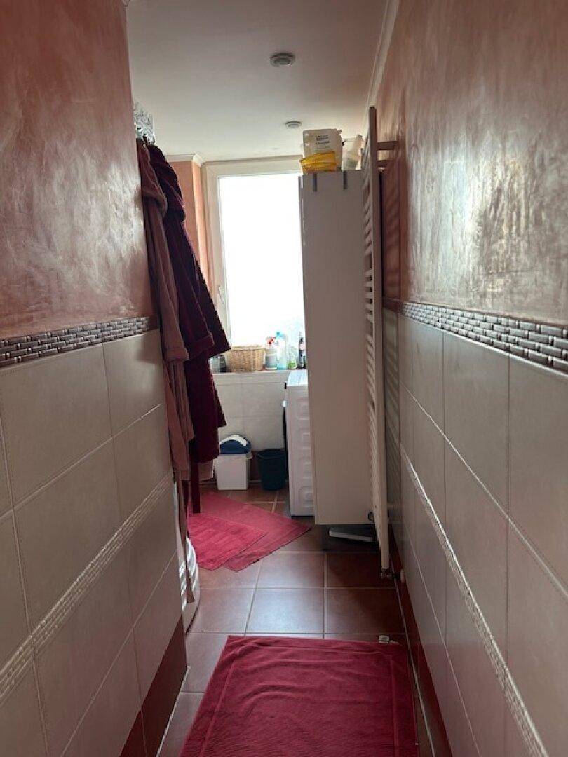 Schmaler Badezimmerbereich mit Waschmaschine, Fenster und Heizkörper.