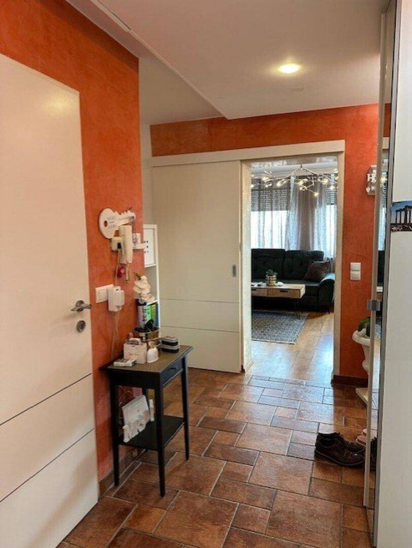 Flur mit Terrakotta-Fliesenboden und Blick durch eine Schiebetür ins Wohnzimmer.