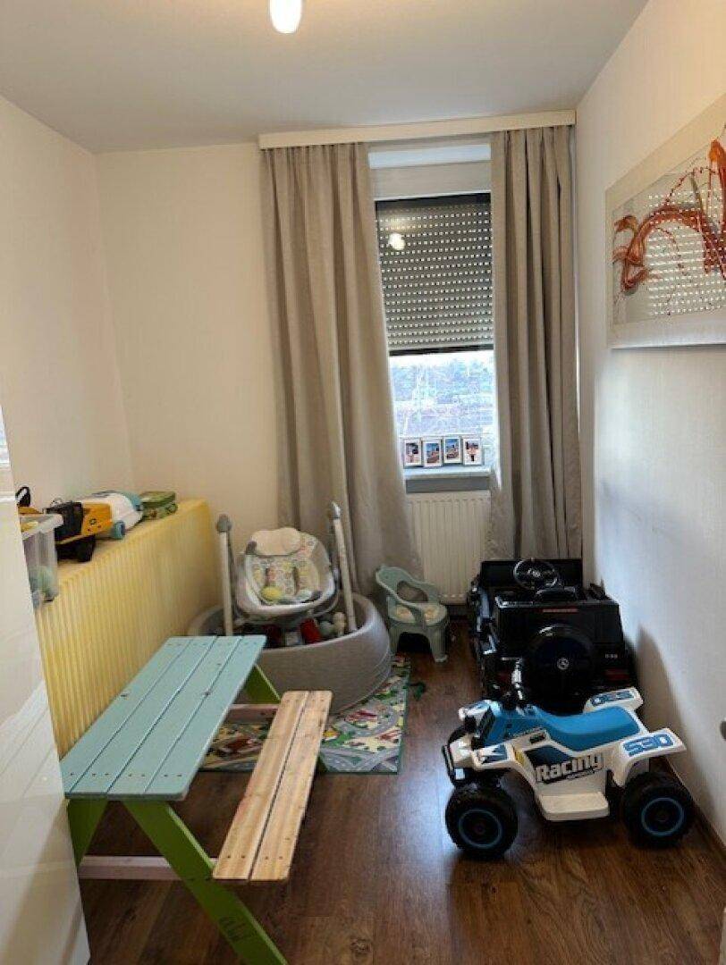 Kinderzimmer mit Spielzeug, kleinem Tisch und Fenster mit Rollladen.