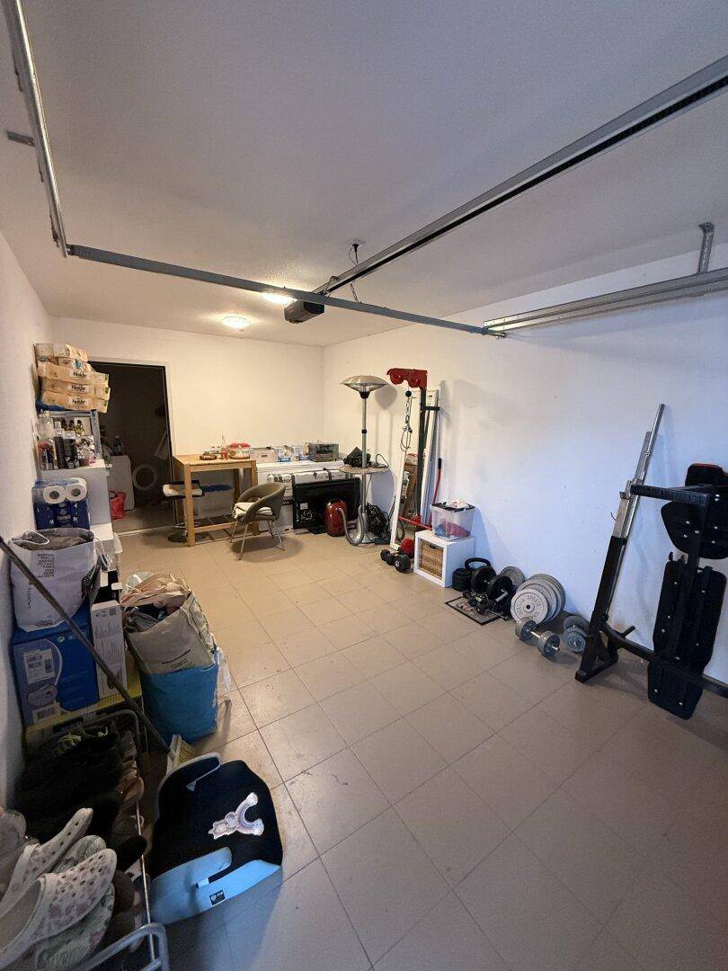 Geräumige Garage mit Fliesenboden, Stauraum und Fitnessgeräten.