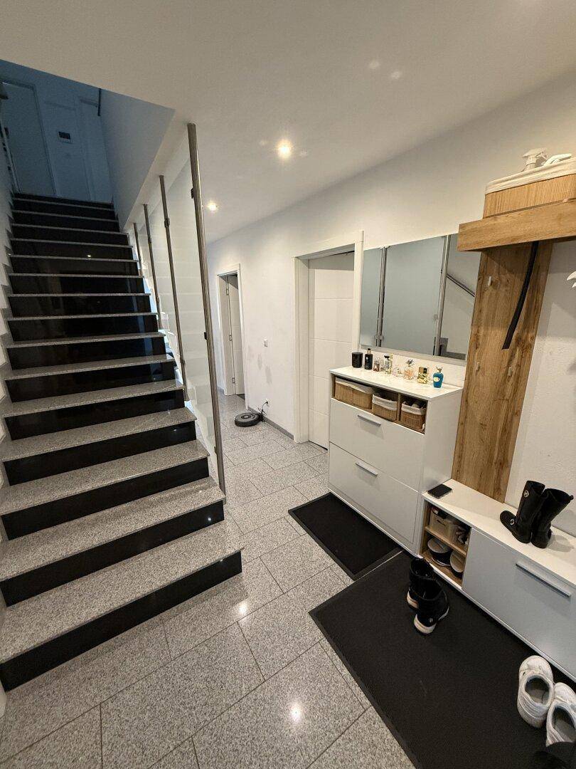 Eingangsbereich mit gefliestem Boden, Treppe und Garderobenmöbeln.