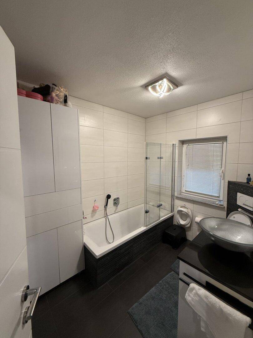 Helles Badezimmer mit Badewanne, Dusche und modernem Waschbecken.