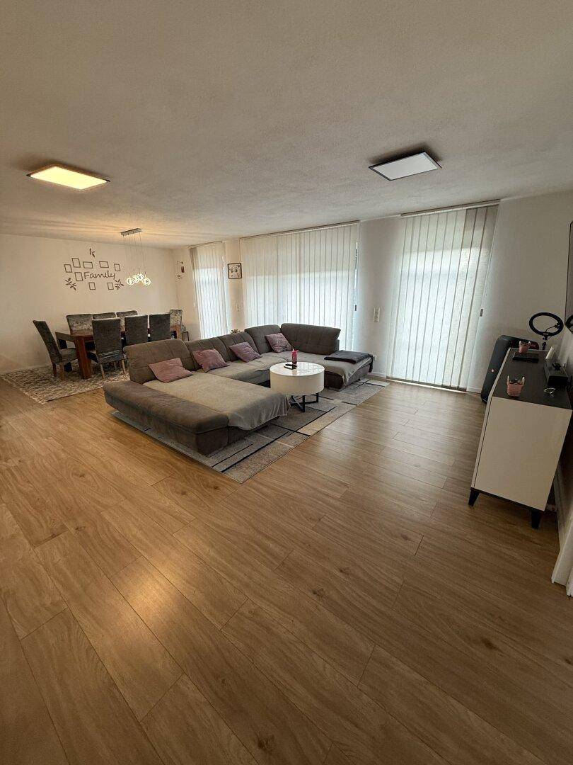 Heller Wohn-Essbereich mit großem Ecksofa, Esstisch und Holzboden.