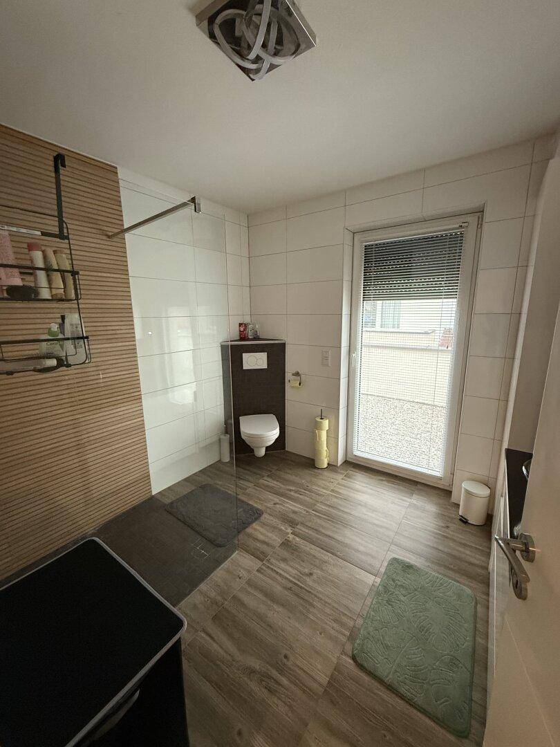 Modernes Badezimmer mit ebenerdiger Dusche, WC und Zugang zur Terrasse.