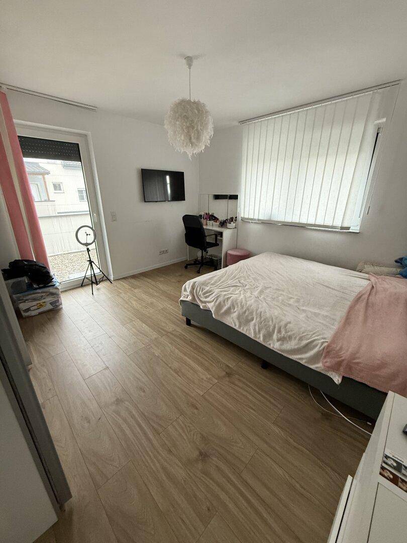Helles Schlafzimmer mit Holzboden, Schreibtisch und Zugang zum Außenbereich.