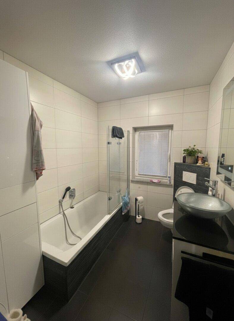 Badezimmer mit Badewanne, Dusche, modernem Waschbecken und Fenster.