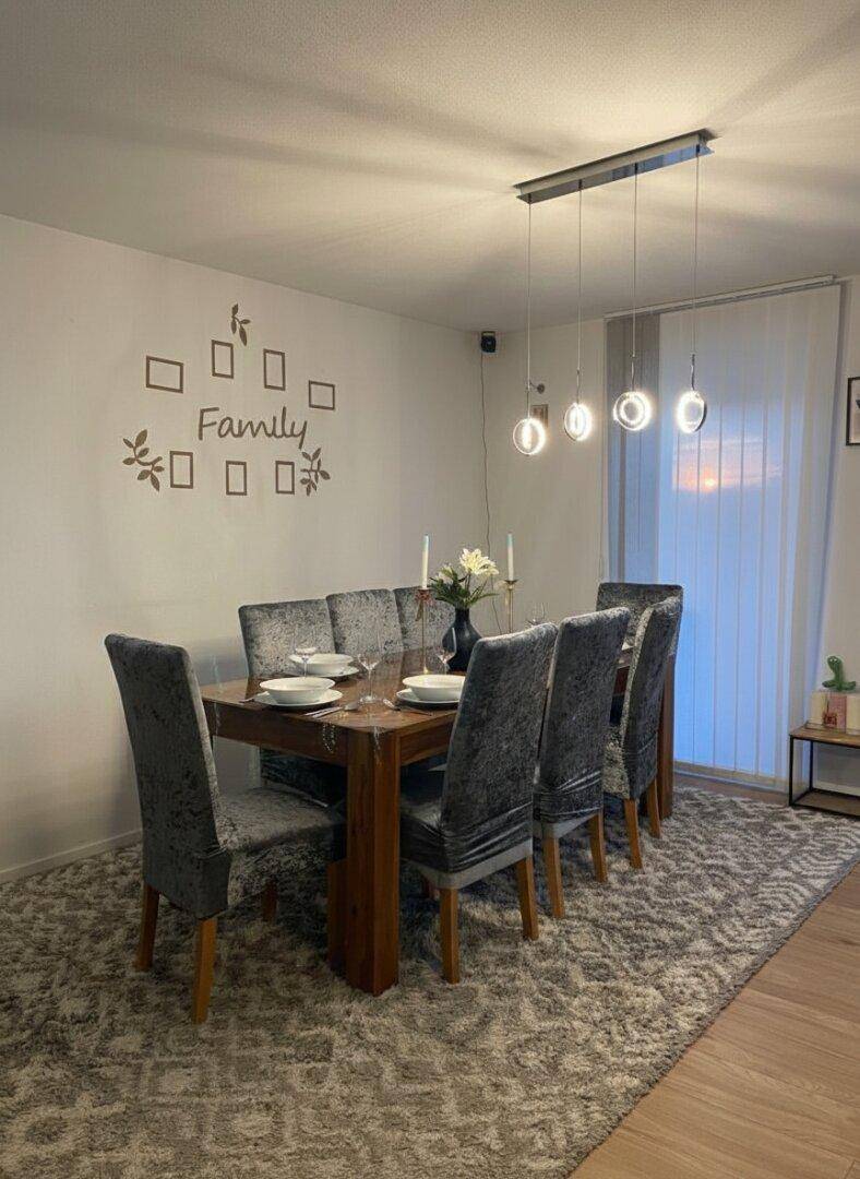 Gemütlicher Essbereich mit großem Holztisch, gepolsterten Stühlen und modernem Licht.