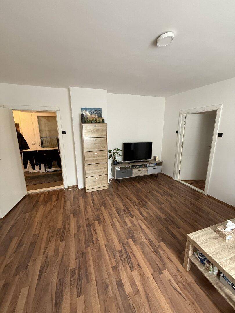 Helles Wohnzimmer mit Laminatboden, TV-Möbeln und Zugang zu weiteren Räumen.
