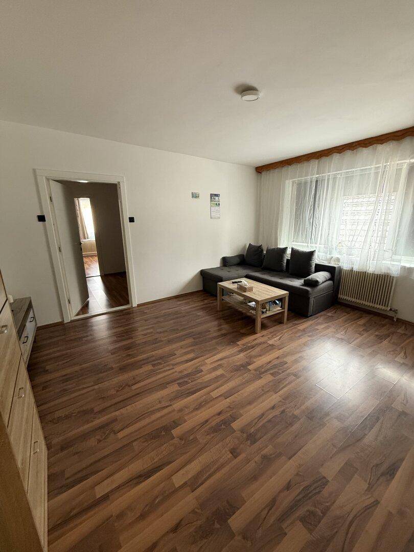 Gemütliches Wohnzimmer mit Laminatboden, Sofa und einem Fenster mit Vorhängen.
