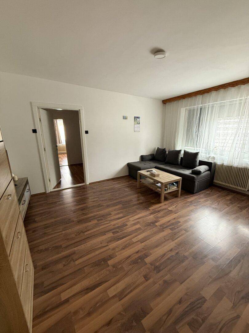 Wohnzimmer mit Laminatboden, bequemer Couch und einem Couchtisch in der Mitte des Raumes.