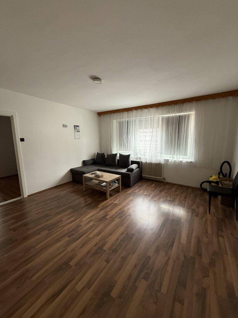 Geräumiges Wohnzimmer mit Laminatboden, Sofa und einem großen Fenster für viel Tageslicht.