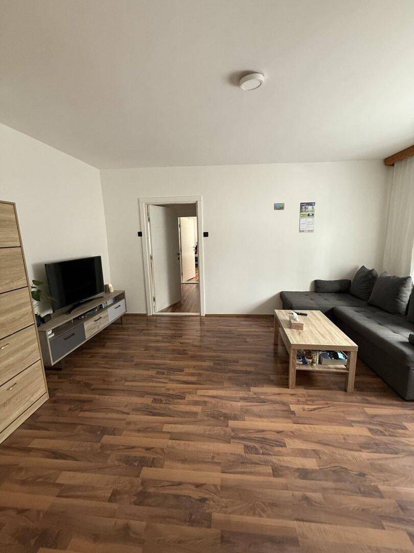 Helles Wohnzimmer mit Laminatboden, TV-Möbeln und einem Sofa, das zum Entspannen einlädt.