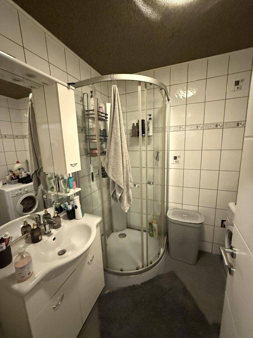 Kleines Badezimmer mit Duschkabine, Waschbecken und Fliesen an den Wänden.