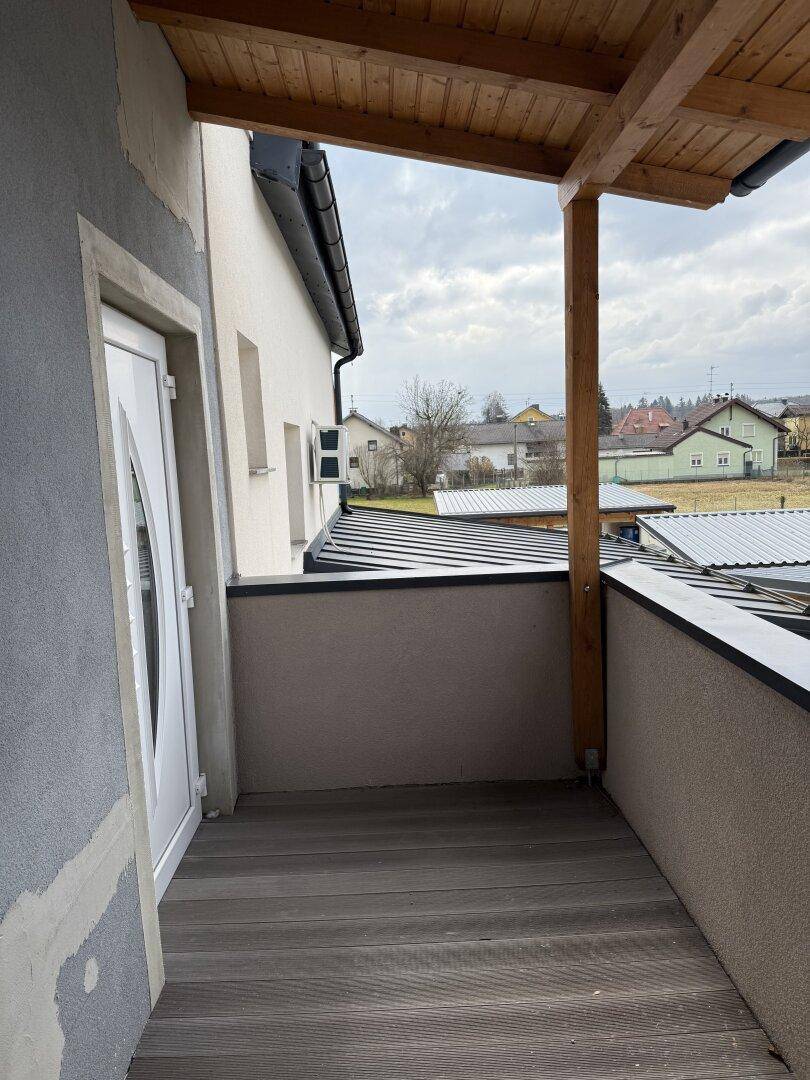 Überdachter Balkon mit Holzboden und Blick auf die umliegende Wohngegend.