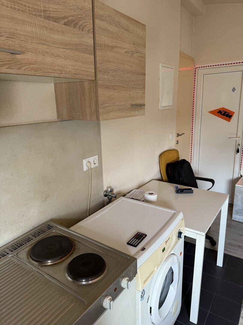 Kleine Küchenzeile mit Kochfeld und Waschmaschine in einem Wohnbereich integriert.