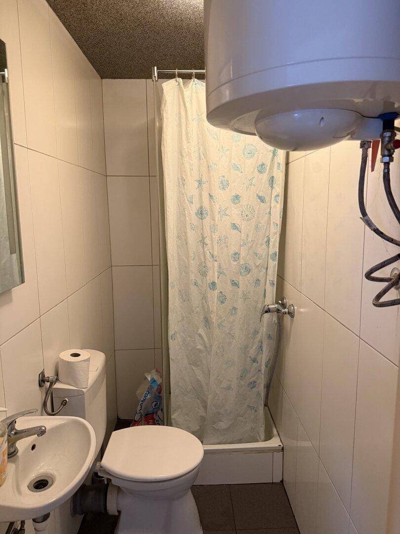 Einfaches Badezimmer mit Dusche, Toilette und Waschbecken, gefliesten Wänden und einem Boiler.