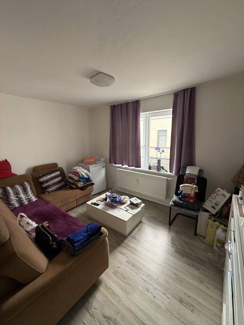 Geräumiges Wohnzimmer mit Sofa, Couchtisch und einem Fenster, das viel Tageslicht hereinlässt.