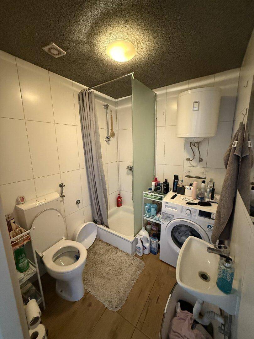 Funktionales Badezimmer mit Dusche, WC, Waschbecken und Waschmaschine, alles auf kleinem Raum.