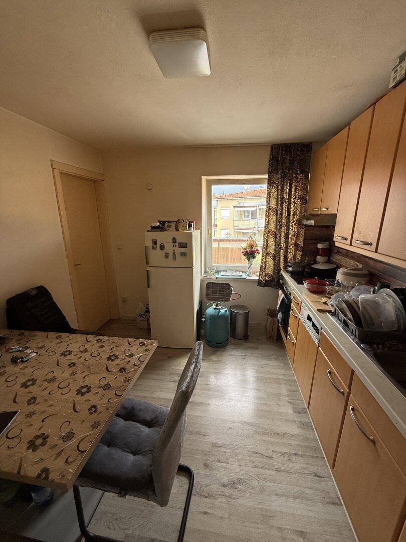 Helle Küche mit Holzschränken, Essbereich und einem Fenster für natürliche Belüftung.