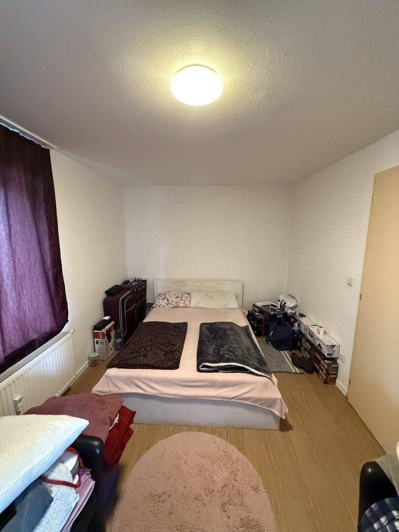 Schlafzimmer mit Doppelbett, hellem Boden und lila Vorhängen, die für Privatsphäre sorgen.