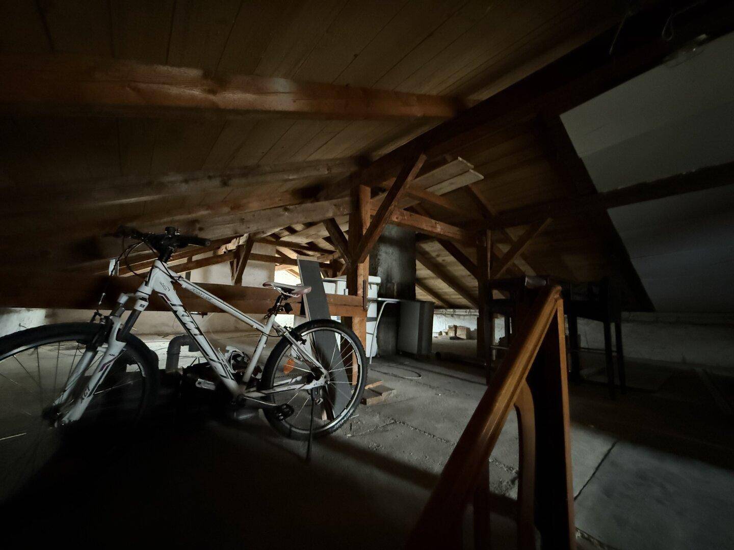Dunkler Dachboden mit sichtbarer Holzkonstruktion und einer abgestellten Fahrrad.