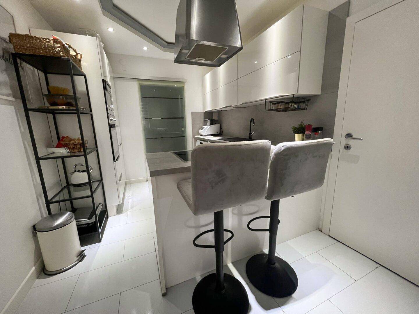 Helle Küche mit Frühstücksbar, modernen Barhockern und integrierter Dunstabzugshaube.