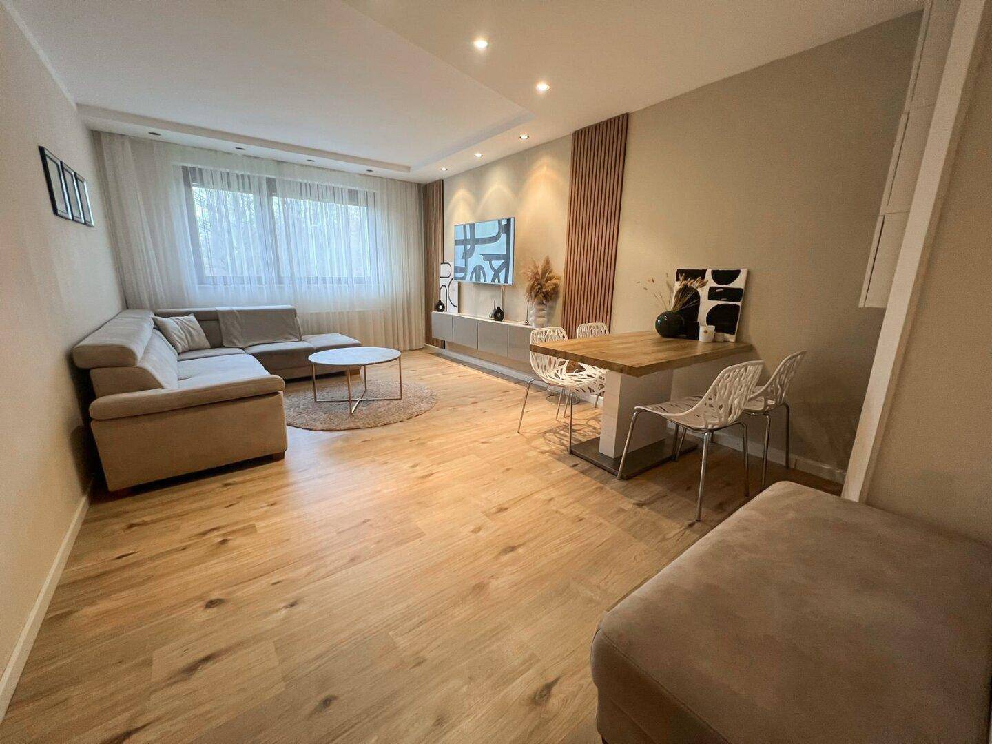 Offener Wohn-Essbereich mit hellem Holzfußboden, bequemer Sitzecke und modernem Esstisch.
