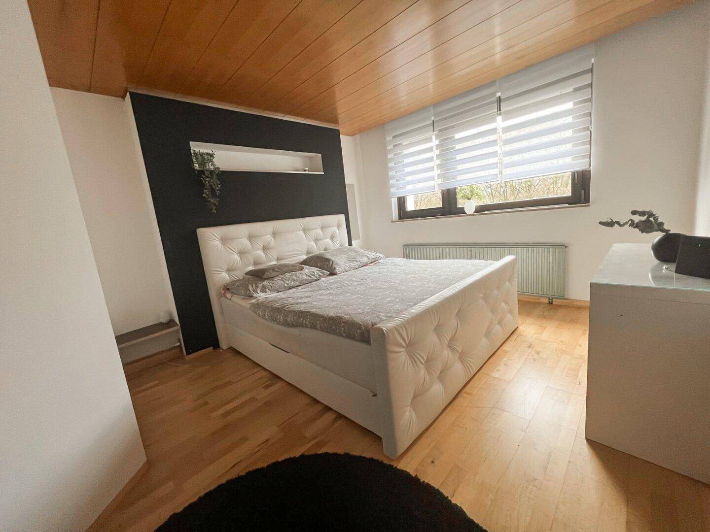 Gemütliches Schlafzimmer mit Holzbalkendecke, großem Bett und Fenster mit Blick ins Grüne.
