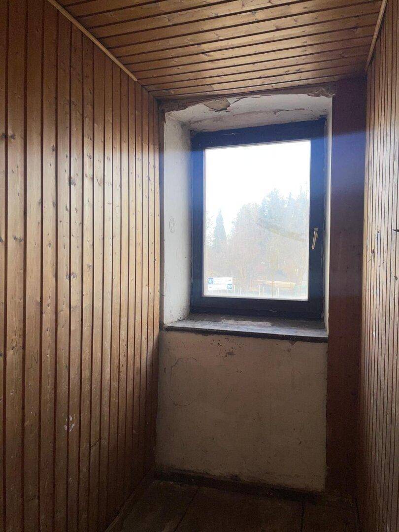 Kleiner Raum mit Holzvertäfelung und einem Fenster, das Tageslicht hereinlässt.