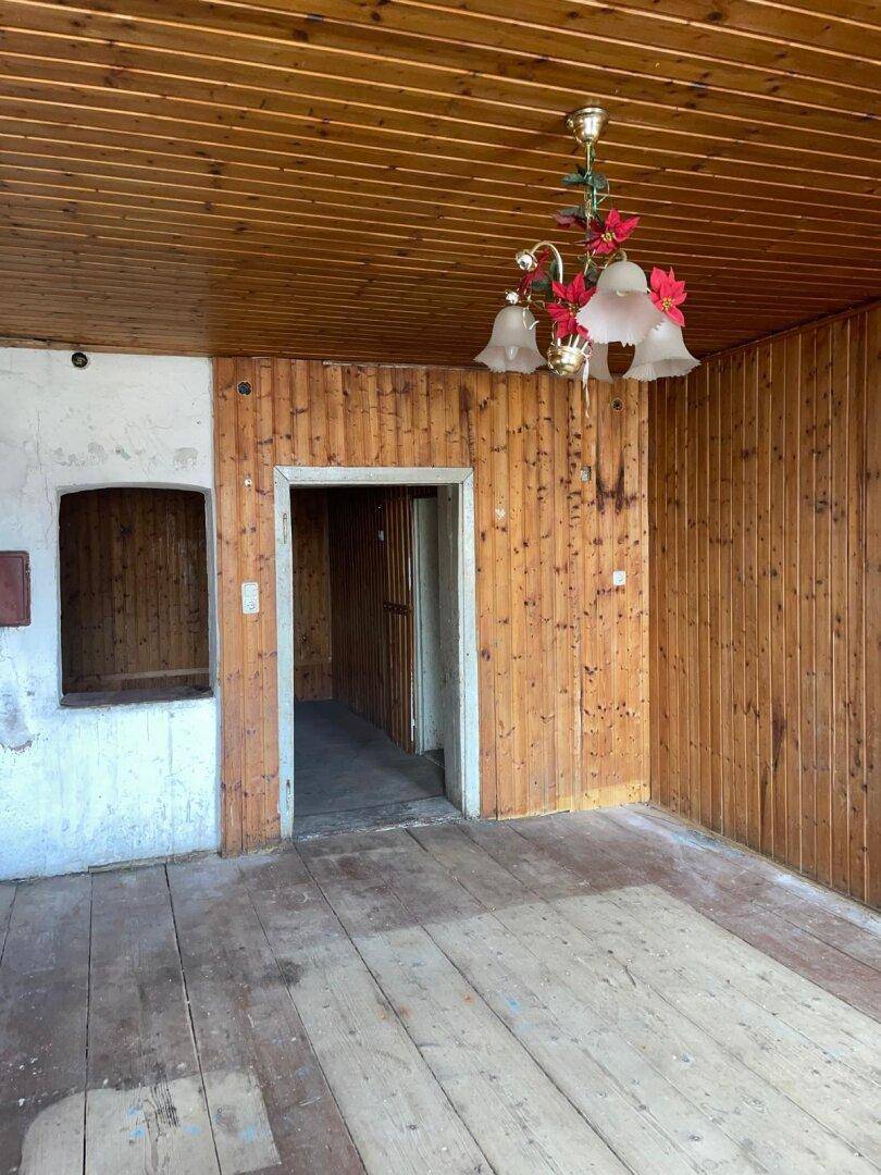 Geräumiger Raum mit Holzvertäfelung, Holzdielenboden und einer dekorativen Deckenleuchte.