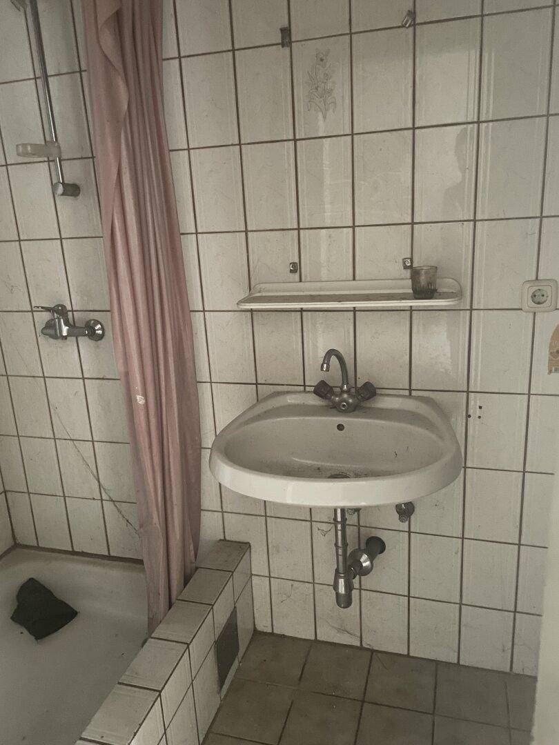 Einfaches Badezimmer mit weißen Fliesen, Waschbecken und einer Badewanne mit Duschvorhang.