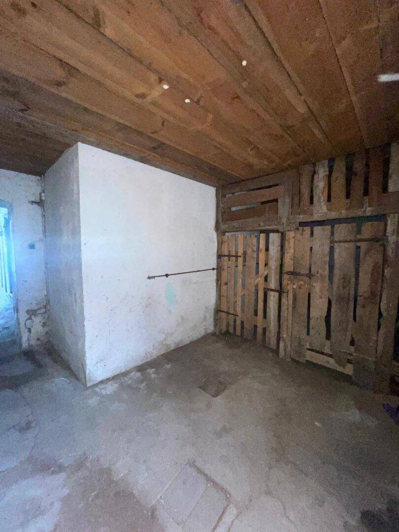 Einfacher Lagerraum mit Holzbalkendecke und provisorischen Holzwänden.