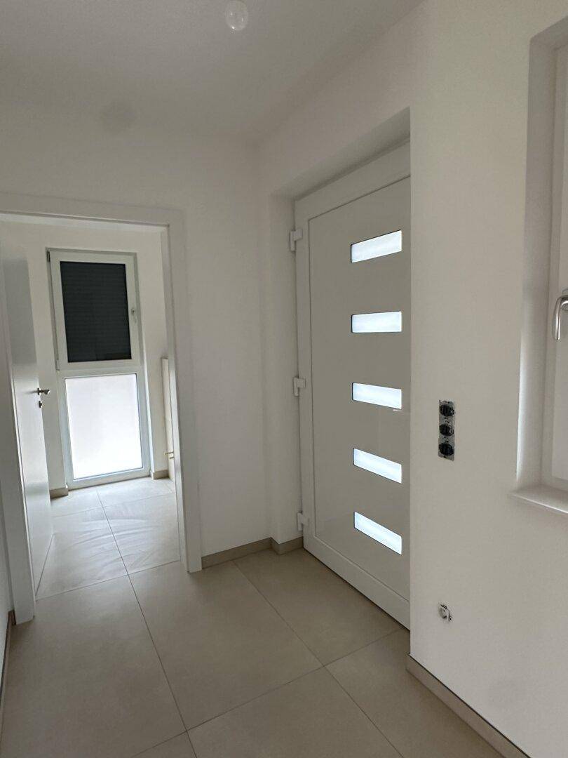 Heller Eingangsbereich mit Fliesenboden und moderner Haustür mit Glaseinsätzen.