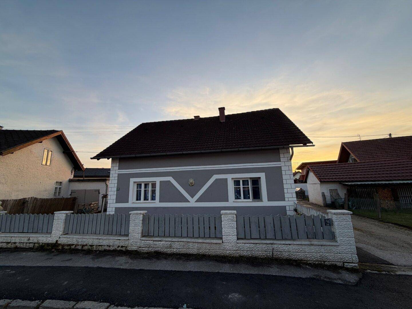 Ansicht des grauen Einfamilienhauses von der Straße mit dekorativem Zaun im Vordergrund.