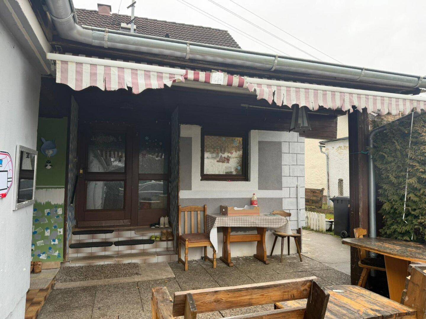 Überdachte Terrasse mit rustikalen Holzmöbeln und Markise, ideal für Mahlzeiten im Freien.