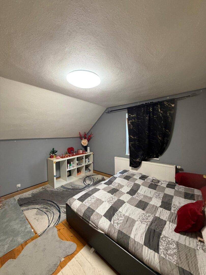 Gemütliches Schlafzimmer im Dachgeschoss mit schrägen Wänden und Teppichboden.