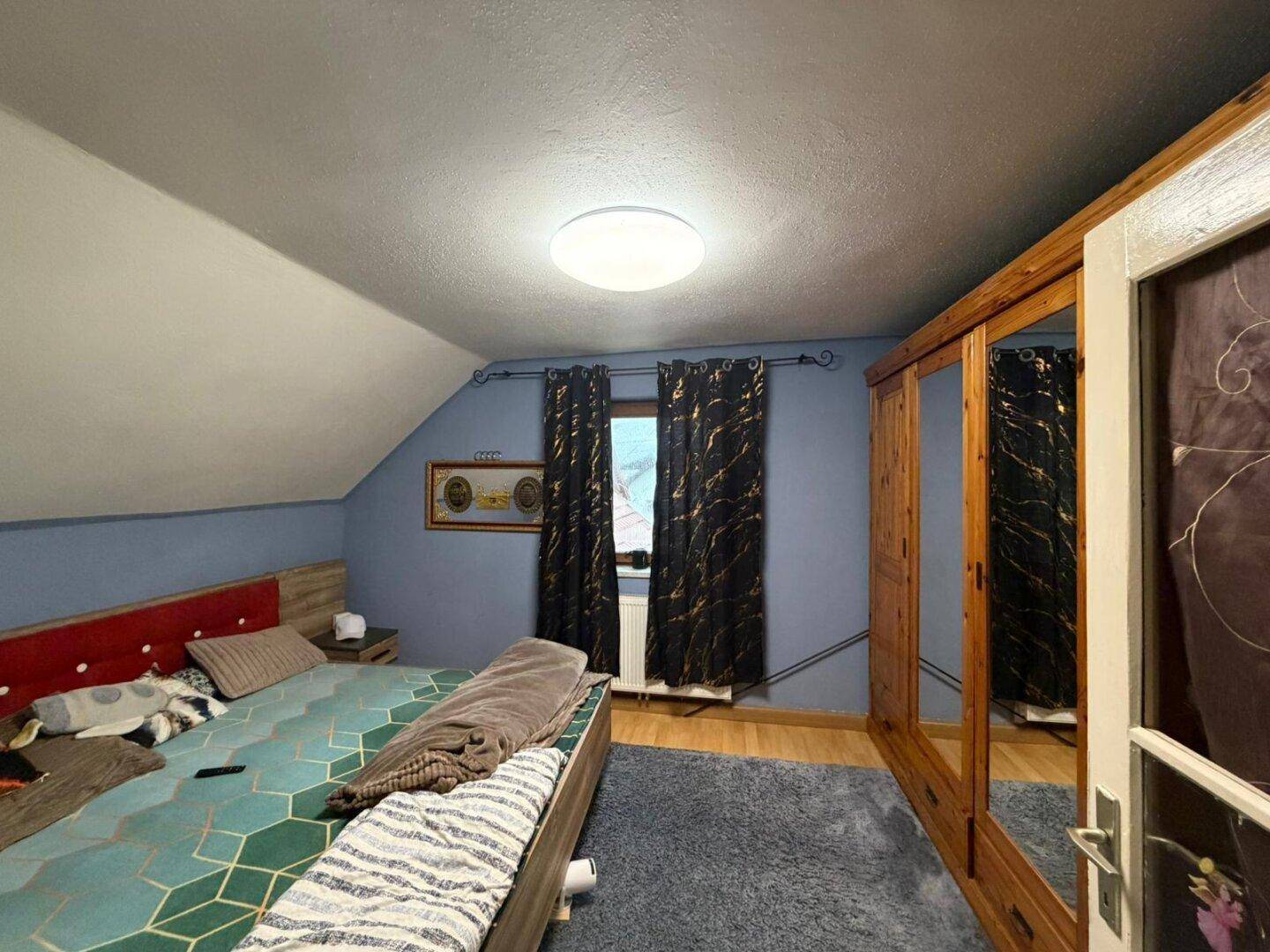 Schlafzimmer mit blauen Wänden, Holzboden und großem Spiegelschrank im Dachgeschoss.