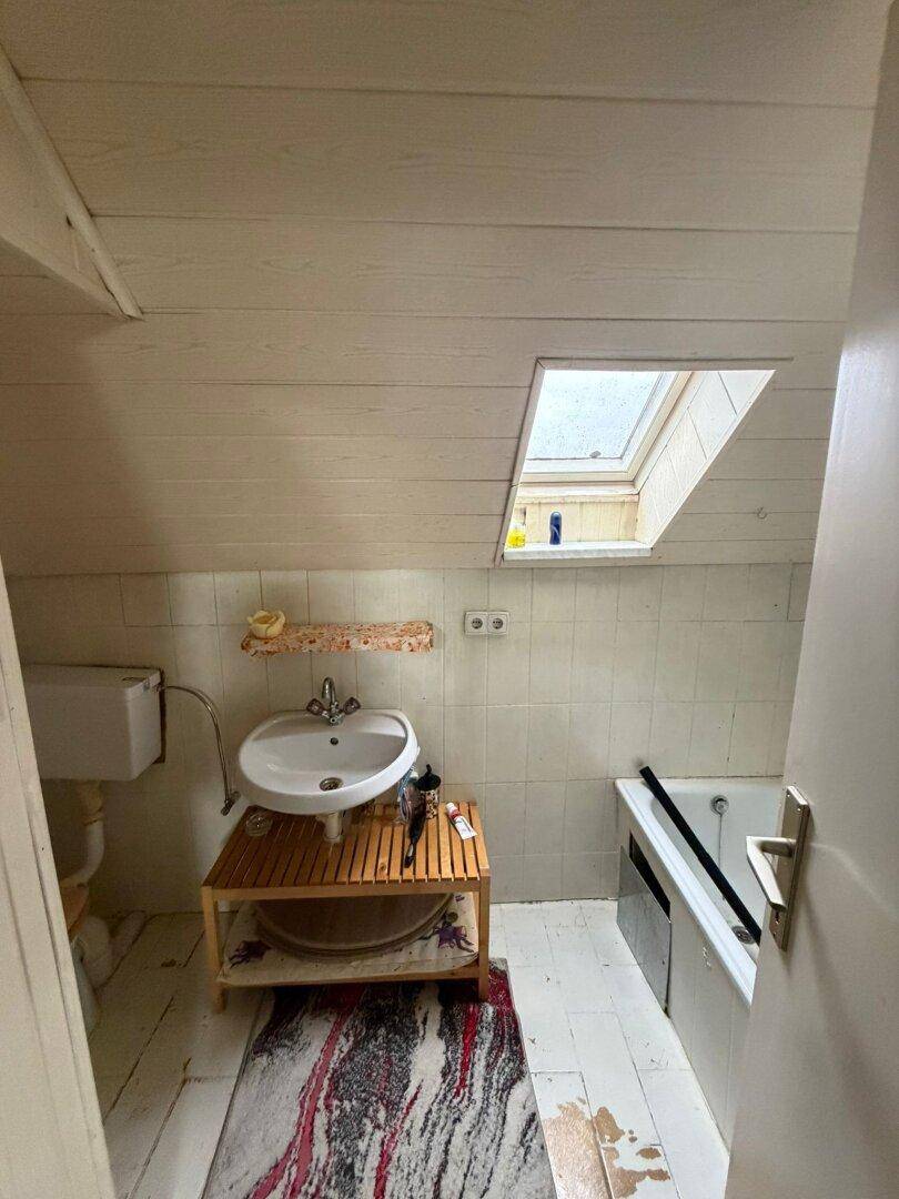 Dachgeschoss-Badezimmer mit Dachfenster, Waschbecken und Badewanne, einfach eingerichtet.