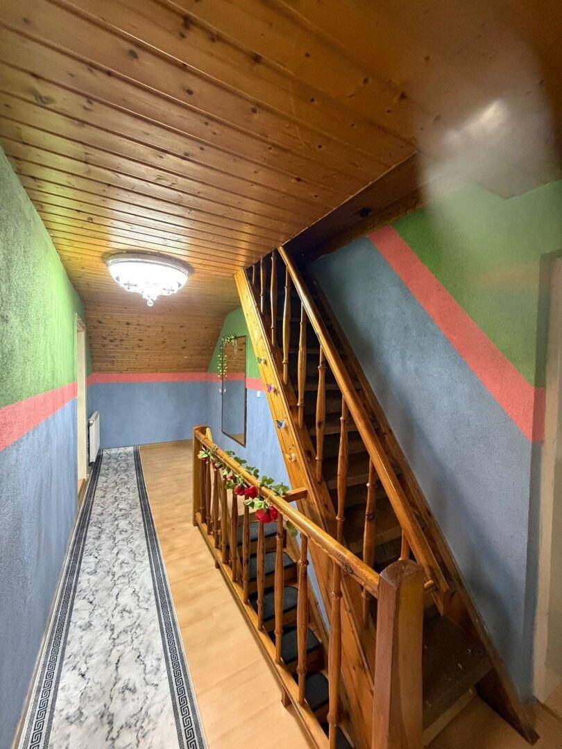 Flur mit Holztreppe und Holzdecke, farbenfroh gestrichenen Wänden und Teppichläufer.