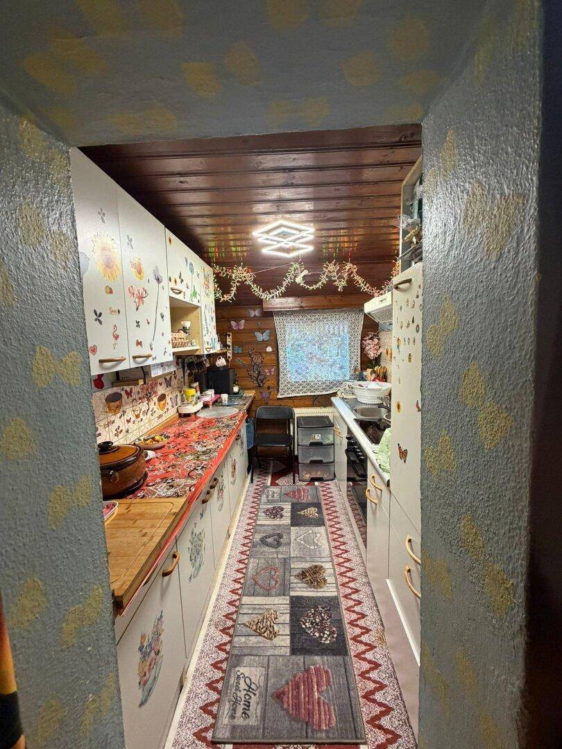 Schmale Küche mit Holzdecke, bunten Schränken und Teppichläufer, funktional eingerichtet.