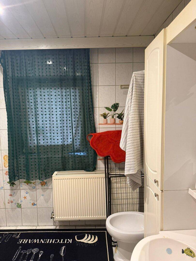 Badezimmer mit Fliesenwänden, Fenster und Bidet, einfach und funktional ausgestattet.