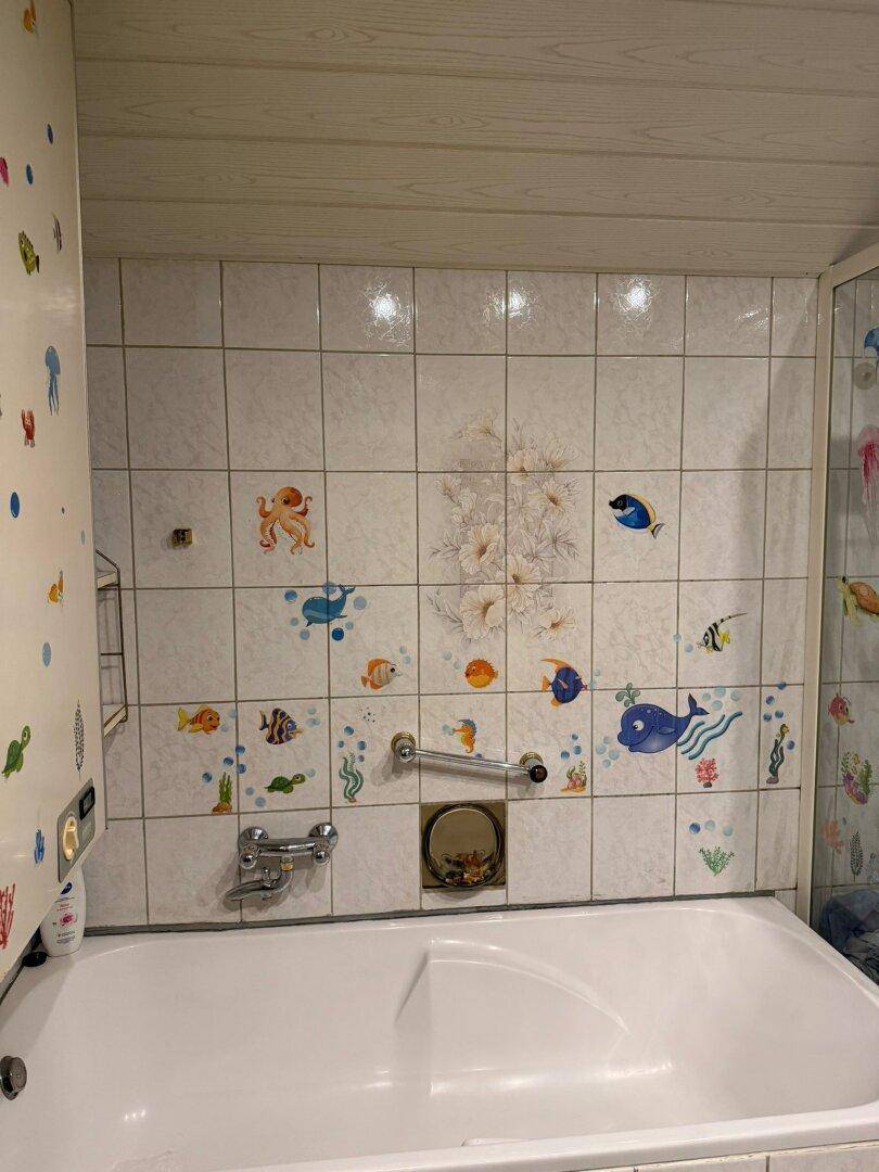 Badezimmer mit Badewanne und verspielten Fliesenstickern, einfach und kinderfreundlich gestaltet.