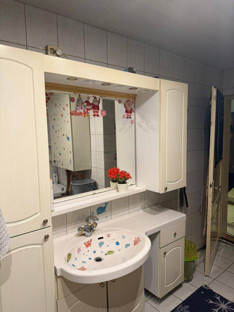 Badezimmer mit Waschbecken, Spiegelschrank und Fliesenwänden, funktional eingerichtet.