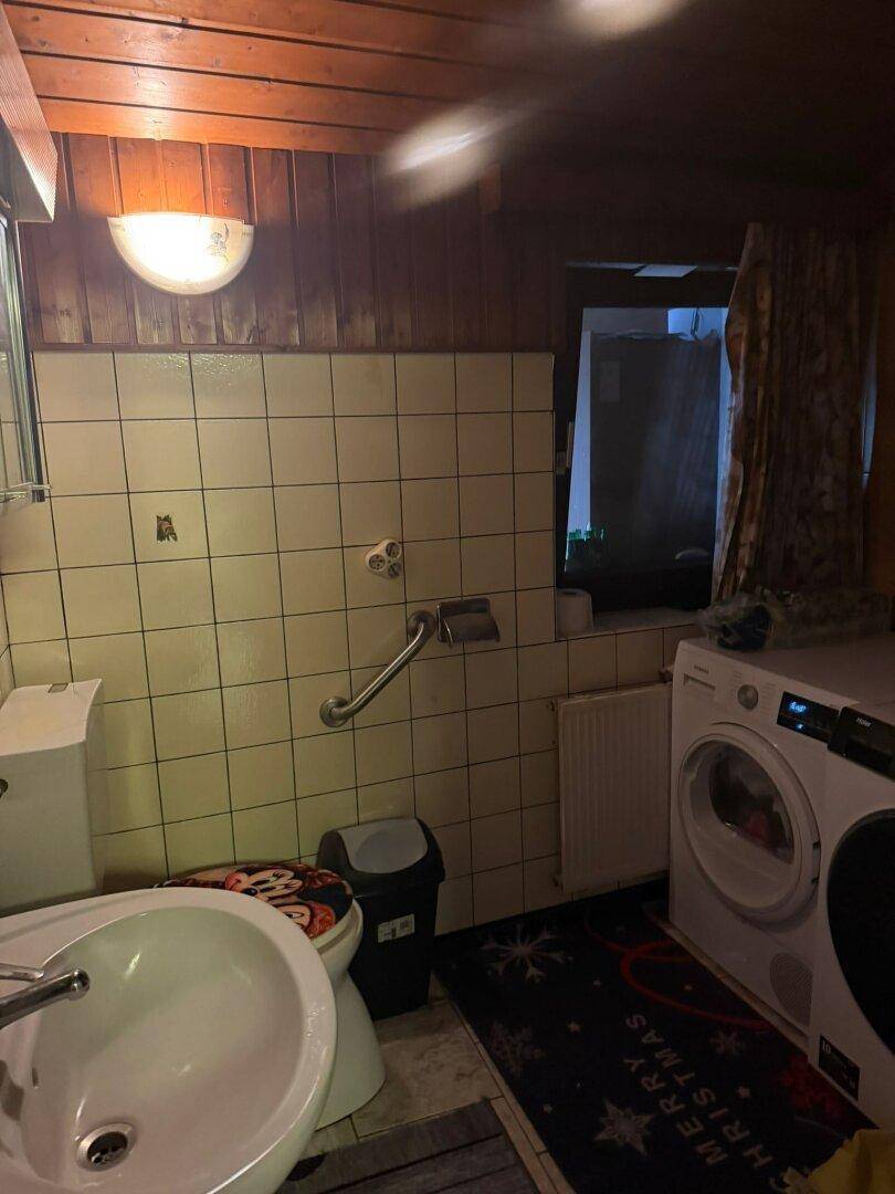 Badezimmer mit Waschmaschine, Trockner und WC, einfach gefliest und funktional.