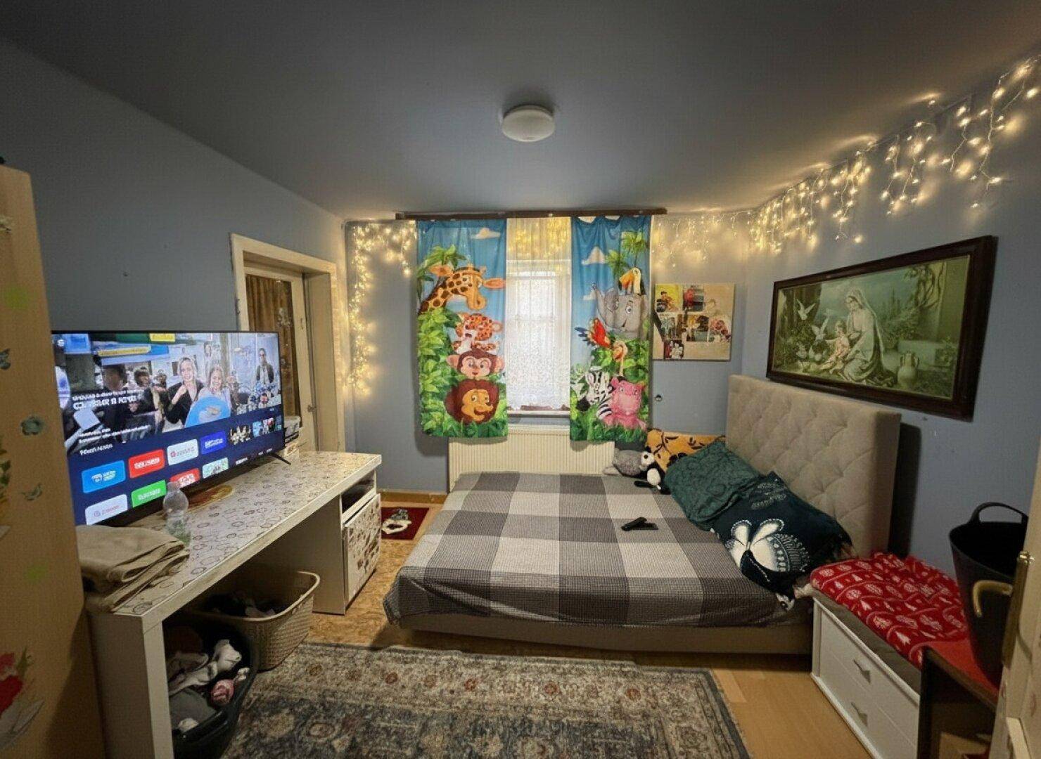 Kinderzimmer mit Bett, Fernseher und Lichterketten, farbenfroh und spielerisch dekoriert.