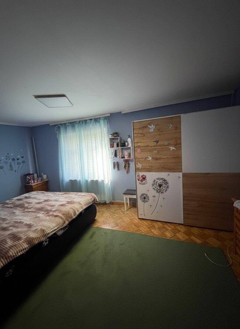 Schlafzimmer mit Holzboden, großem Schrank und Fenster, in hellblauen Tönen gehalten.